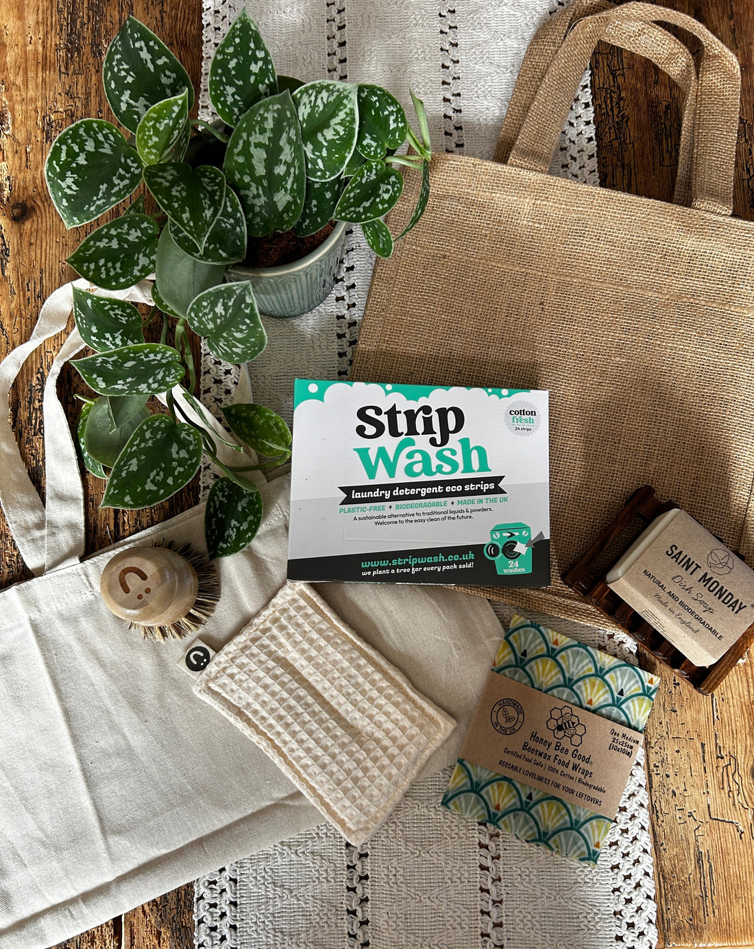 Eco-friendly cleaning products and reusable bags for sustainable living with plant on wooden table.