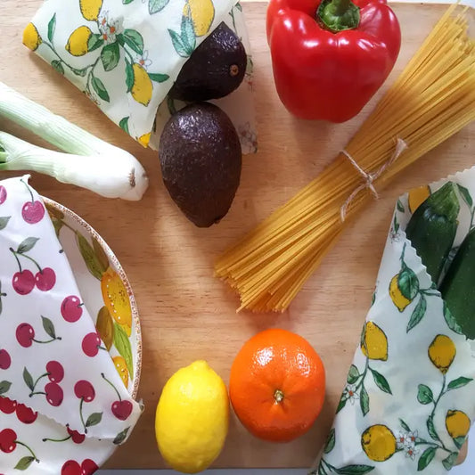 Fresh vegetables and pasta on a wooden board with eco-friendly beeswax wraps, showcasing sustainable kitchen essentials.