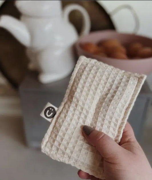 Person holding a handmade dish sponge by Moonie, designed for tough dirt and grime, with a background of kitchen items.